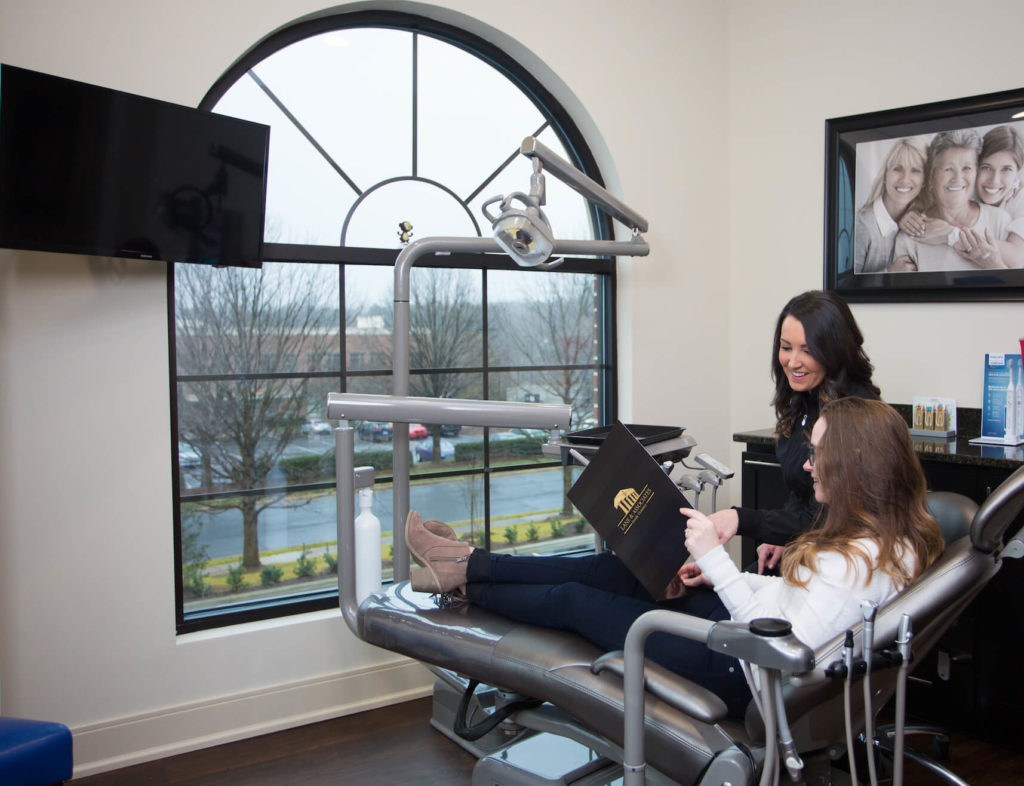 Patient in dental chair holding folder talking to assistant about dental treatment