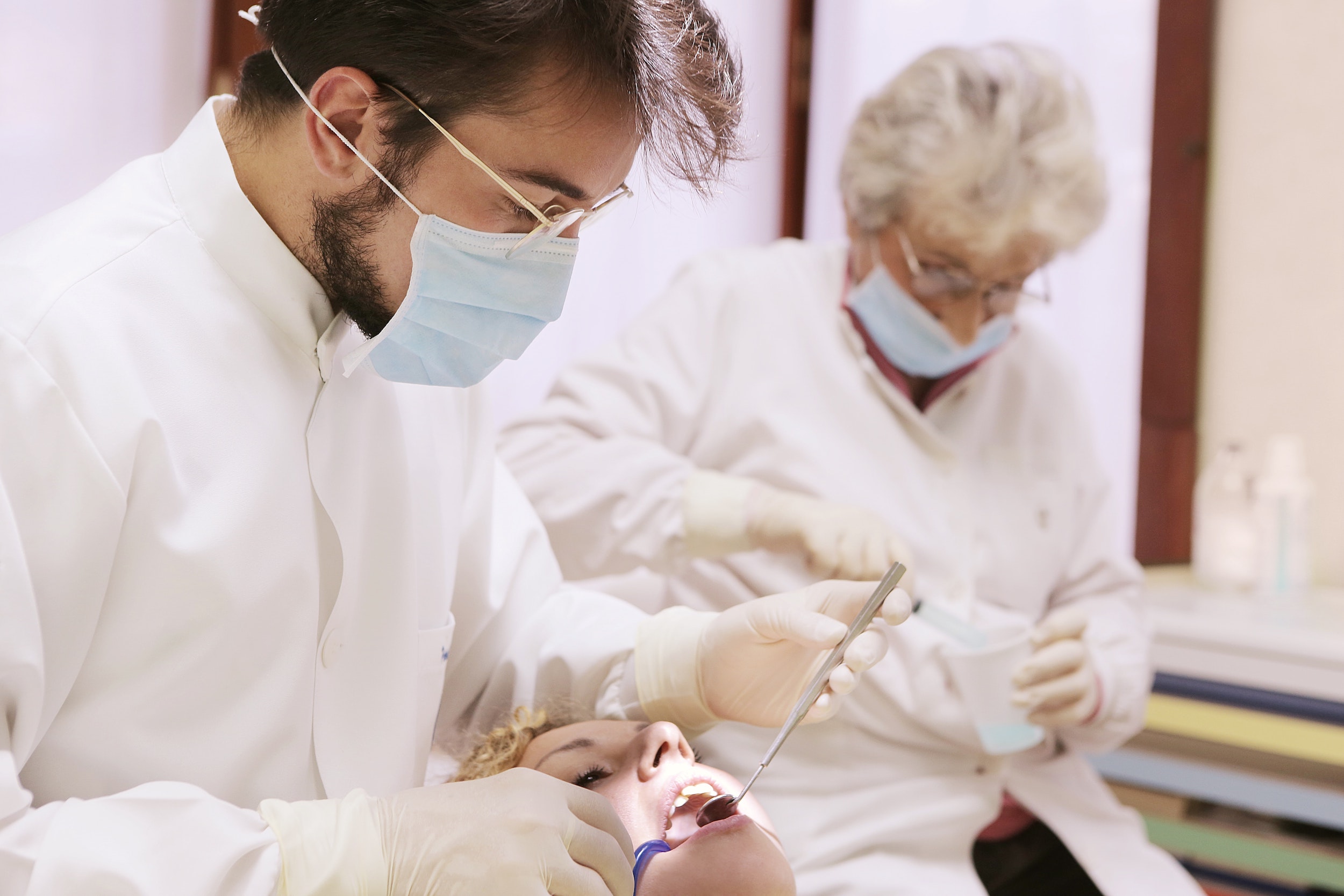 dentist with mask cleaning woman's teeth