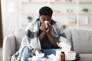 Sick black guy sitting at couch, sneezing