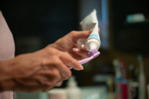 Closeup view of a woman squeezing a toothpaste tube to put it on toothbrush in a home bathroom.